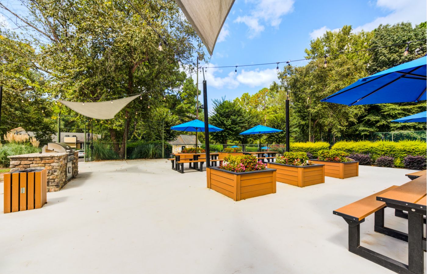 Sunny courtyard with shade sails, blue umbrellas, and wooden planter boxes at Madison Laurel Oaks apartments in Raleigh, NC