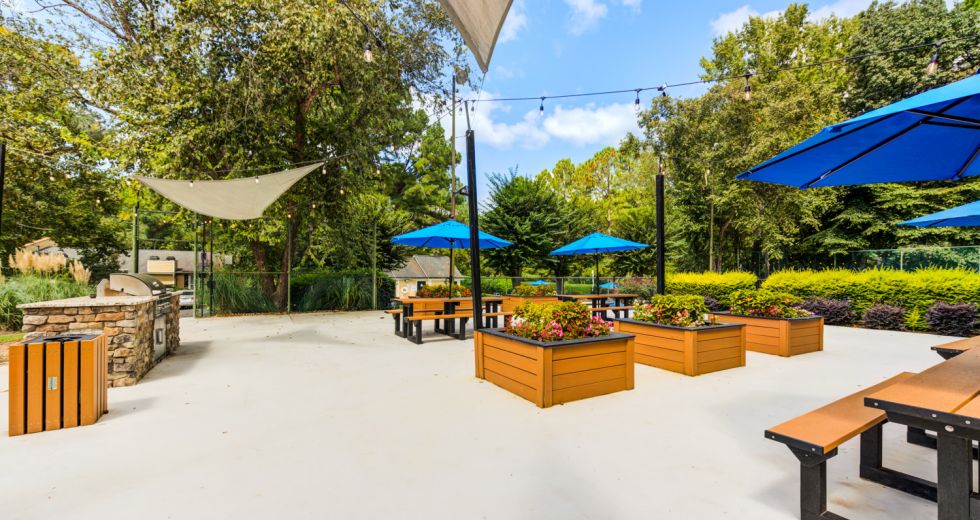 Sunny courtyard with shade sails, blue umbrellas, and wooden planter boxes at Madison Laurel Oaks apartments in Raleigh, NC