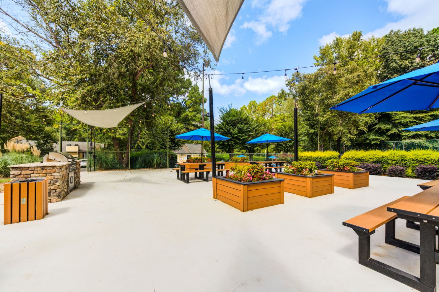 Sunny courtyard with shade sails, blue umbrellas, and wooden planter boxes at Madison Laurel Oaks apartments in Raleigh, NC