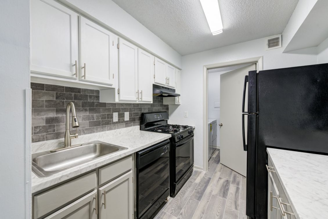 Updated kitchen with two-tone white and grey cabinetry, black appliances, and tile backsplash at Madison Laurel Oaks apartments in North Raleigh, NC