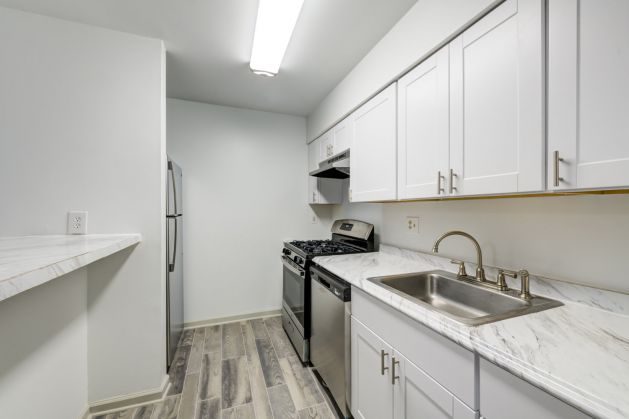 Updated galley kitchen with white cabinetry, black appliances, tile backsplash, and wood-style flooring at Madison Laurel Oaks apartments in North Raleigh, NC