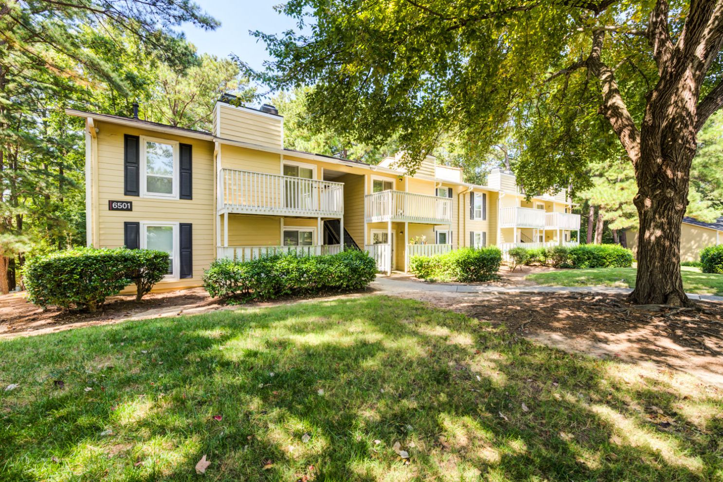 Yellow and cream exterior of Madison Laurel Oaks apartment buildings with lush green lawn and mature trees in North Raleigh, NC