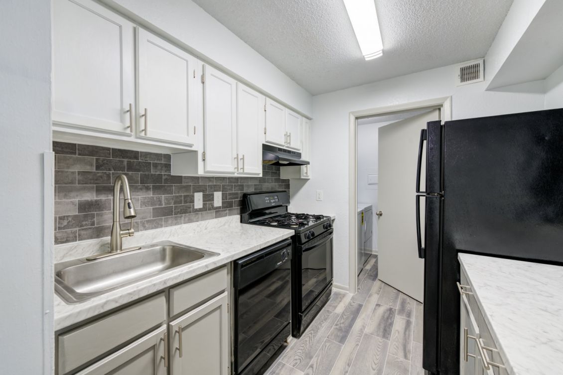 Updated kitchen with two-tone white and grey cabinetry, black appliances, and tile backsplash at Madison Laurel Oaks apartments in North Raleigh, NC
