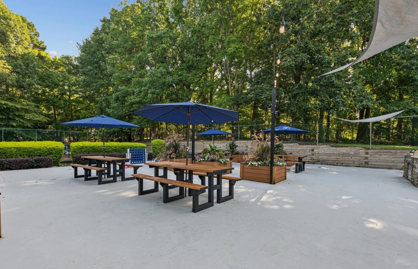 Outdoor patio area with multiple picnic tables under blue umbrellas and string lights.