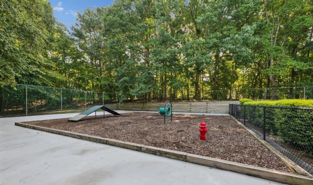 Fenced dog park with agility equipment, wood chips, and a red fire hydrant.